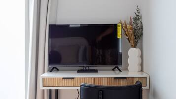 A modern room with a wooden desk, a flat-screen TV, a black chair, and a small potted plant.