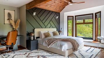 A bedroom with a bed, a desk, a chair, and a window with a view of trees.