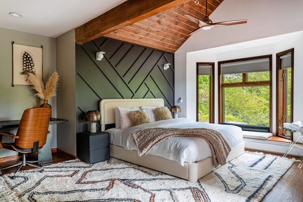 A bedroom with a bed, a desk, a chair, and a window with a view of trees.