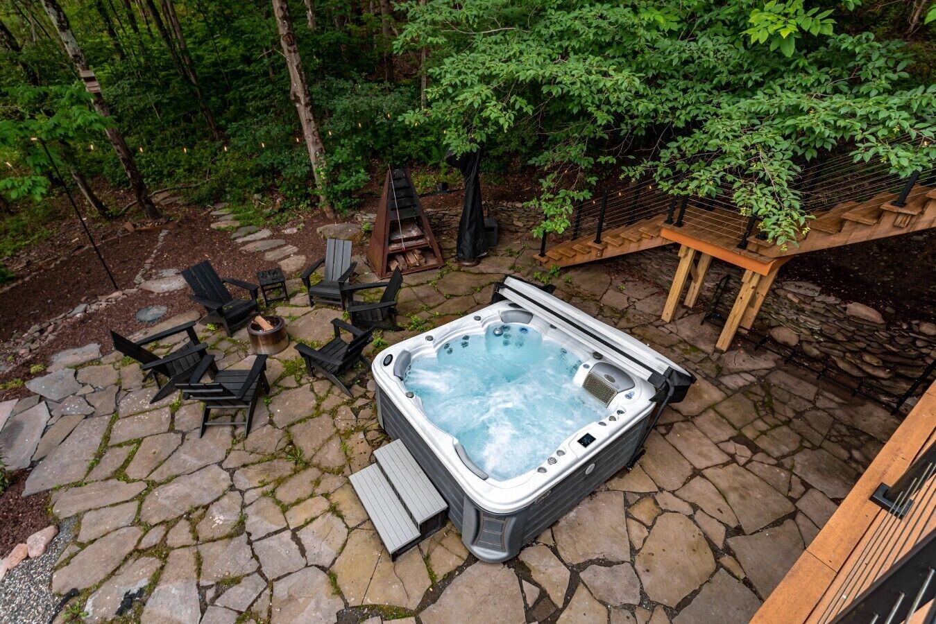 Un bain à remous entouré d’une terrasse en pierre, de coins salon extérieurs et d’une plateforme en bois.