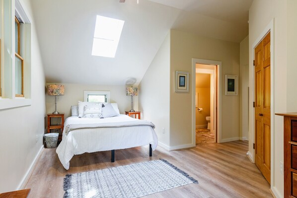 A bedroom with a bed, bedside lamps, a window, and a door leading to a bathroom.