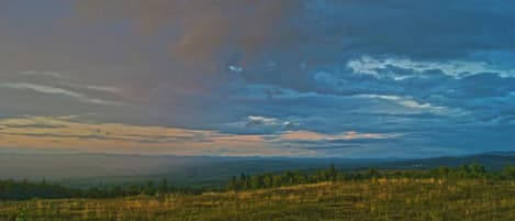 A landscape with a field and distant hills under a cloudy sky.
