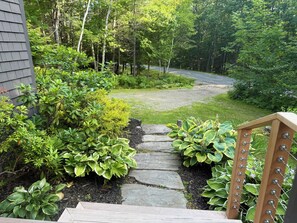 A stone pathway leading to a wooden deck with a view of a forested area. - Peaceful 2 Bedroom Cottage Beside an Organic Blueberry Hill in Hope. (Hope)