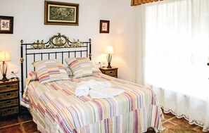 A neatly made bed with a striped bedspread, two bedside lamps, and framed artwork on the walls. - Amazing home in Benalub Casas Viejas (Benalub Casas Viejas)