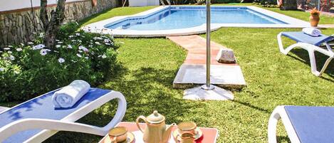 A backyard with a swimming pool, lounge chairs, and a table with a teapot and cups.