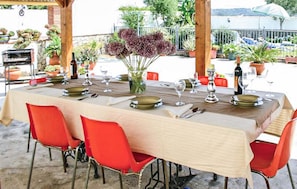 An outdoor dining area with a table set for four, surrounded by red chairs, and a view of the sea in the background. - Amazing home in Benalub Casas Viejas (Benalub Casas Viejas)