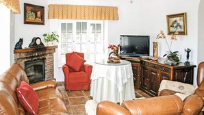 A living room with leather sofas, a red armchair, a fireplace, a television, and various decorative items. - Amazing home in Benalub Casas Viejas (Benalub Casas Viejas)