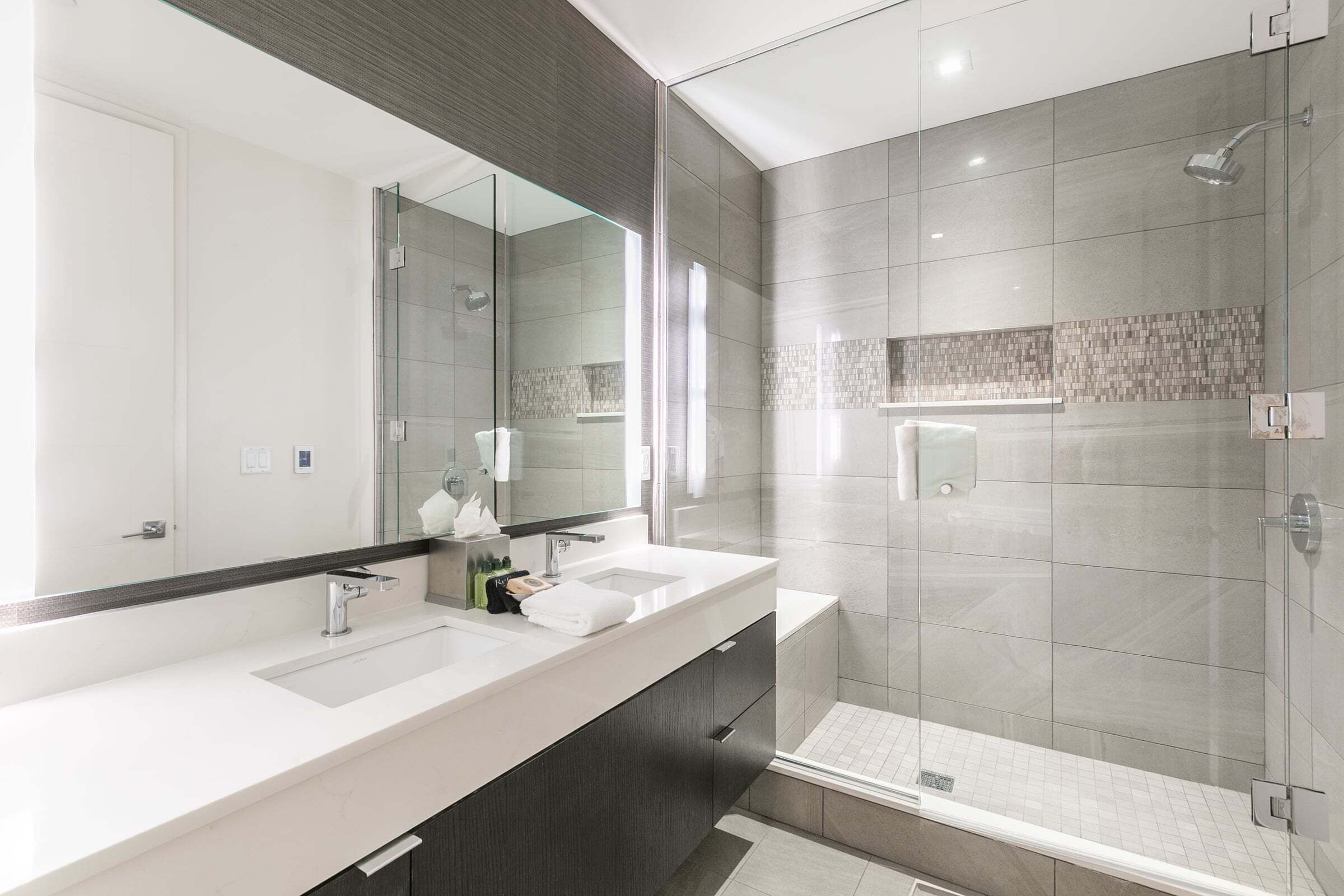 A modern bathroom with a glass-enclosed shower, a large mirror, and a dual sink vanity.
