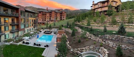 A resort with a swimming pool, outdoor seating, and a hot tub surrounded by a landscaped garden.