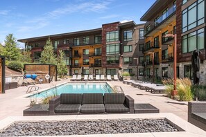A modern building with a pool, outdoor seating, and a stone facade. - True Ski In /Out Lift 2 BD Epic Views, Amazing Amenities; Steps to Gondola (Park City)