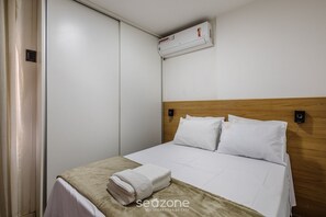 A hotel room with a bed, a wall-mounted air conditioner, and a neatly folded towel on the bed. - Studio With gym and Coworking! Pks0205 (Guará)