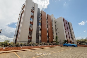 A multi-story residential building with a parking area in front. - Studio With gym and Coworking! Pks0205 (Guará)