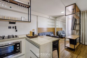 A modern kitchen with a built-in oven, a coffee machine, and a breakfast bar. There is a seating area with a sofa and a table. - Studio With gym and Coworking! Pks0205 (Guará)