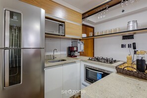 A modern kitchen with a stainless steel refrigerator, microwave, and oven. There is a sink, a coffee maker, and a gas stove. - Studio With gym and Coworking! Pks0205 (Guará)