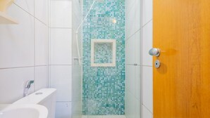 Een badkamer met een douchecabine van glas, een wit toilet en een houten deur.