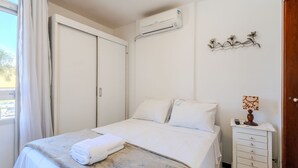 Een hotelkamer met een bed, een nachtkastje met een lamp, een wandairconditioner en een decoratief kunstwerk aan de muur.
