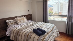 A hotel room with a bed, a window with curtains, a wooden floor, and a ceiling light. - Beautiful 2-bedroom apartment perfect for a relaxing getaway. (Wanchaq)