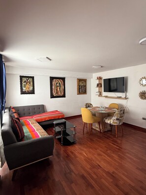 Uma sala de estar moderna com sofá, mesa de centro, mesa de jantar com cadeiras e uma TV de tela plana fixada na parede.