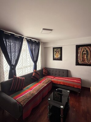 A modern living room with a sectional sofa, a glass coffee table, and two framed religious artworks on the wall. - Beautiful 2-bedroom apartment perfect for a relaxing getaway. (Wanchaq)