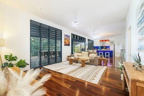 A modern living room with a sofa, coffee table, and a view of the outdoors through large glass doors. - Golden Sands Retreat (Wagait Beach)