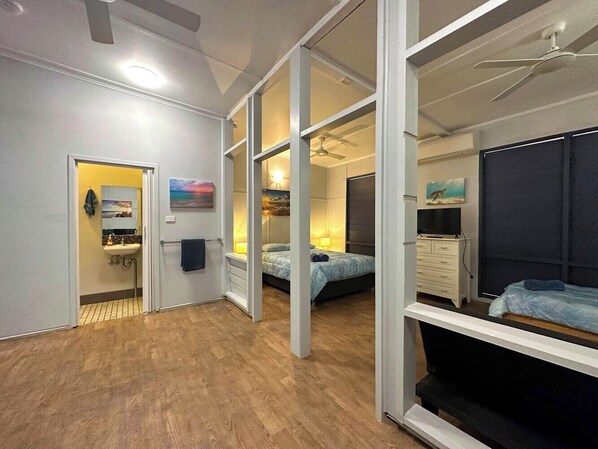 A bedroom with a bed, a dresser, a TV, and a bathroom with a sink and mirror.