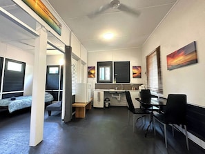 A compact room with a kitchenette, a dining area, and two single beds.