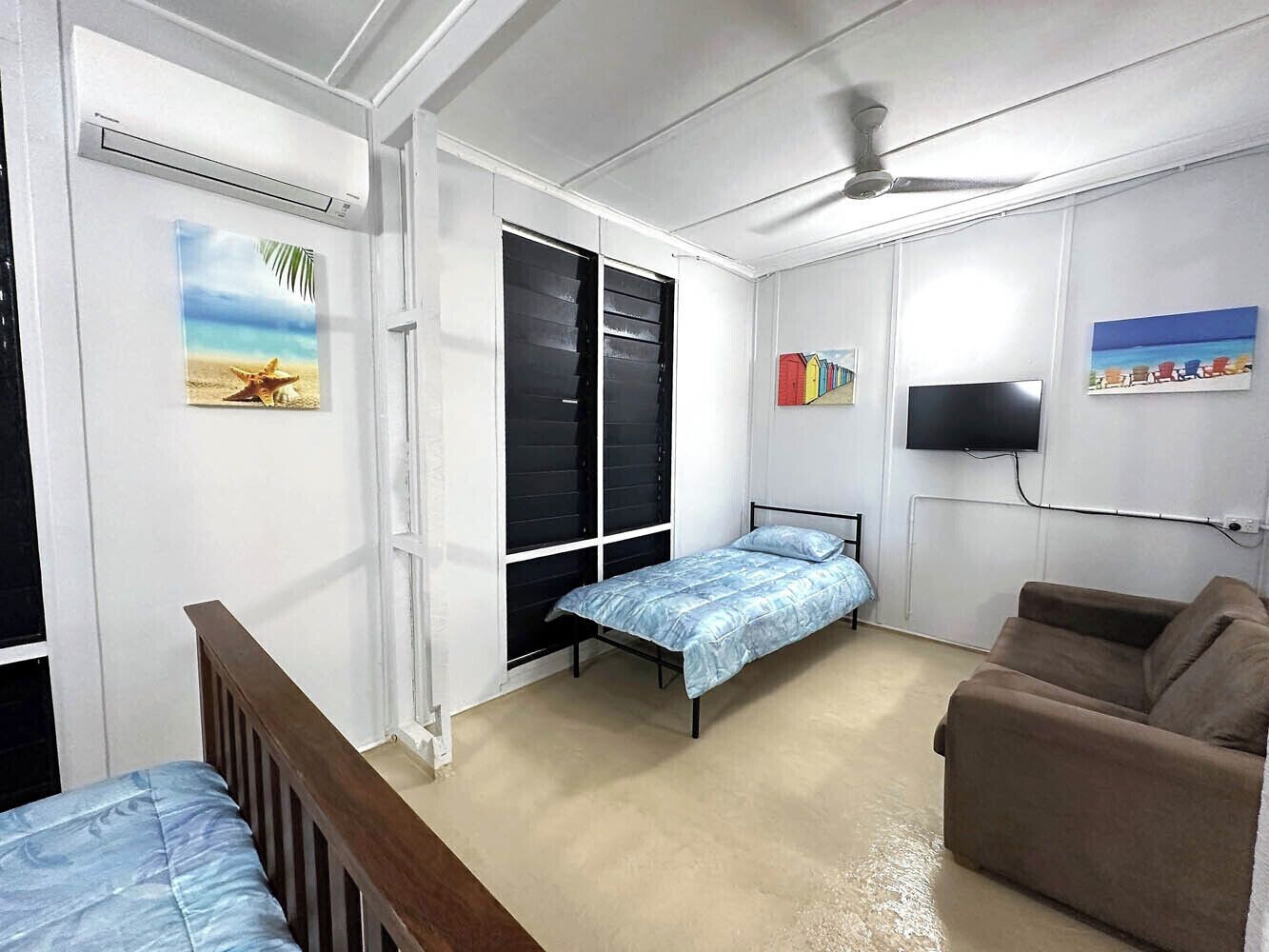 A bedroom with a bed, a sofa, a TV, and a window with blinds.