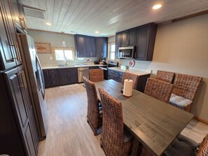A modern kitchen with dark cabinets, a large island, and wicker chairs. - Accomodates up to 15 People (Port O`Connor)