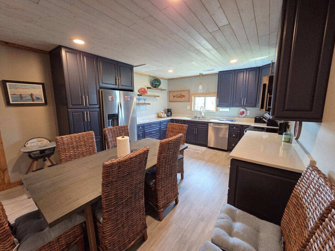A modern kitchen with dark cabinets, a dining area with wicker chairs, and a central island.