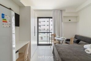 Quarto de hotel moderno com cama, escrivaninha, cadeira, mesinha e varanda com vista para a cidade.