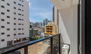 Uma varanda com vista para um horizonte urbano, incluindo um edifício branco com várias janelas e um edifício amarelo com design singular.
