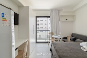 Quarto de hotel moderno com cama, escrivaninha, cadeira, mesinha e varanda com vista para a cidade.