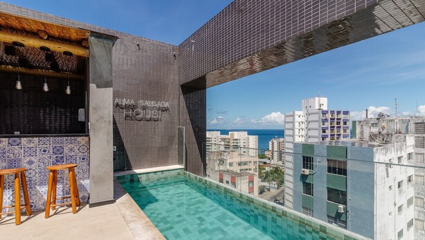 Una piscina en la azotea con vistas a la ciudad y al océano, un área de bar con taburetes, y un letrero que dice "ALMA SALGADA HOUSES".