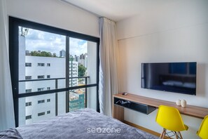 A modern hotel room with a large window, a bed, a TV, a desk, and two yellow chairs. - Modern Studio w/ Pool 450m From the Beach Prv1003 (Salvador)