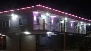 Un edificio de dos plantas con un balcón, una puerta de garaje y una tira de luz de neón roja.