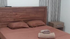 Un dormitorio con una cama de madera, una mesita de noche, una obra de arte circular en la pared y una ventana con cortinas.