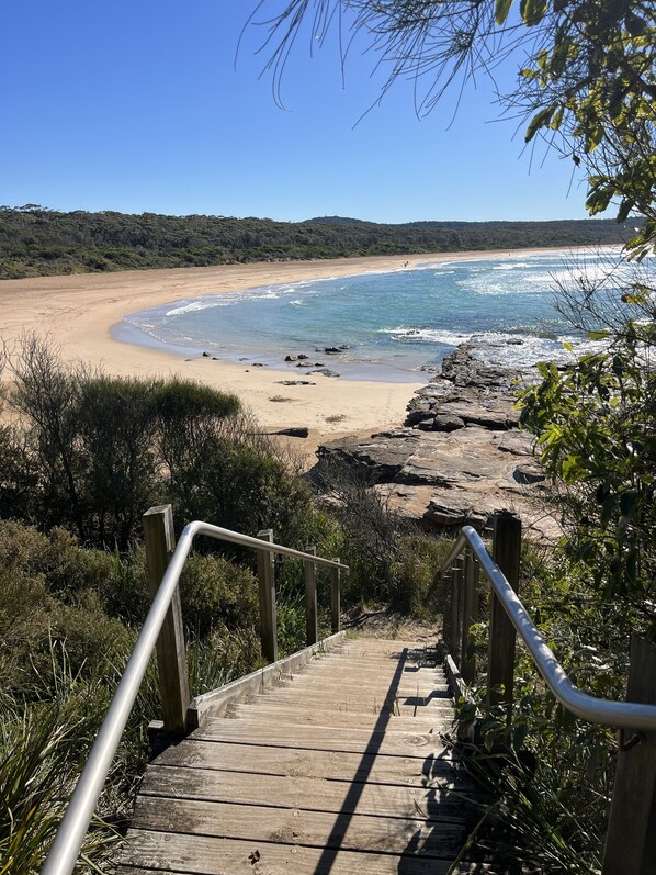 A wooden staircase leading to a beach with a clear view of the ocean and a sandy shoreline.