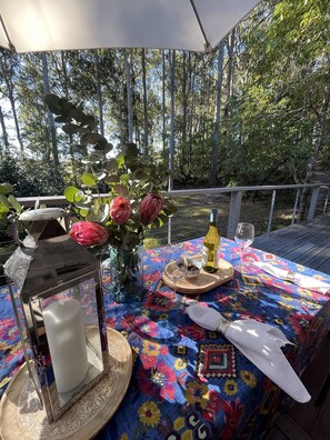 An outdoor dining area with a table set for two, a lantern, and a vase with flowers.