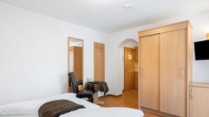 Ein Hotelzimmer mit zwei Betten, einem Schreibtisch, einem Stuhl, einem Kleiderschrank und einem Fernseher.