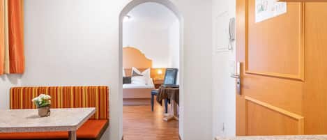 A hotel room with a kitchenette, a dining area with a bench, and a bed with a nightstand.