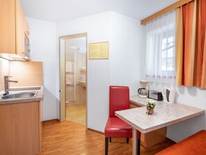 Eine kompakte Küche mit Spüle, einem roten Stuhl, einem kleinen Tisch und einem Fenster mit Vorhängen.
