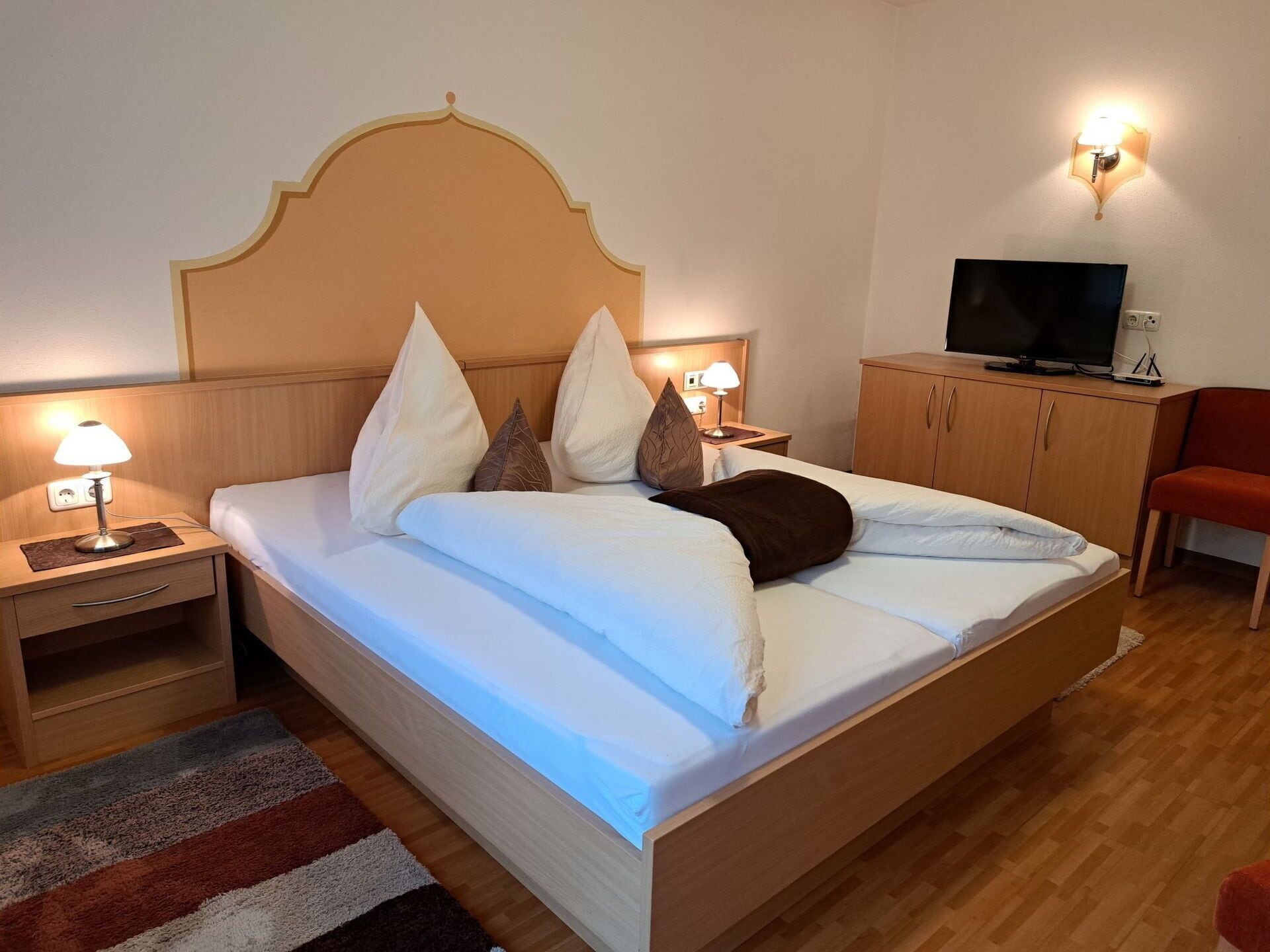 Ein Hotelzimmer mit einem Bett, Nachttischlampen, einem Fernseher und einem Holzschrank.