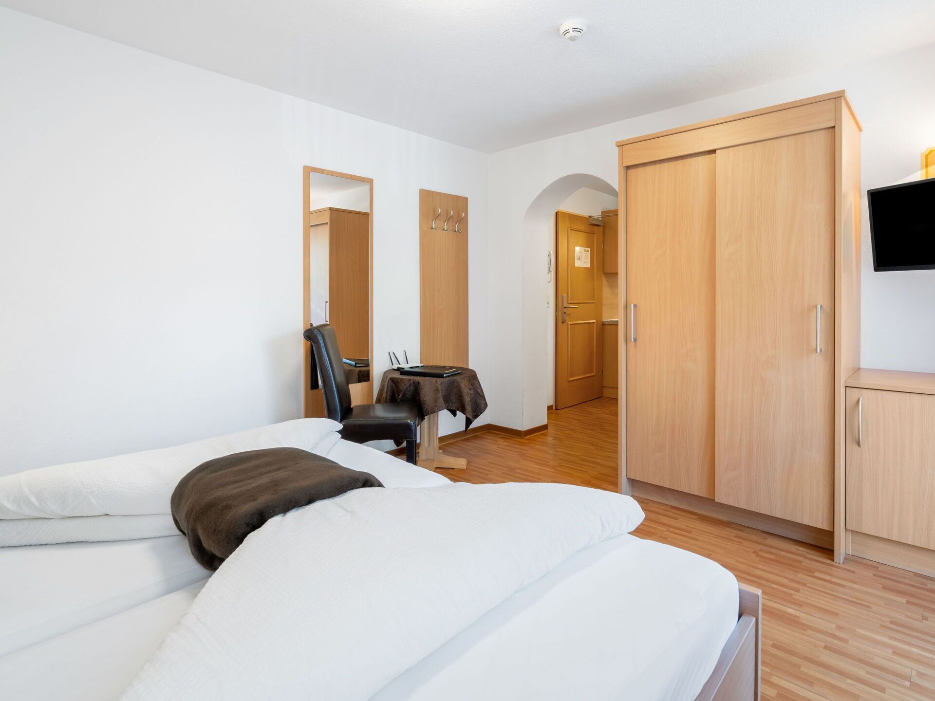 A hotel room with two beds, a desk, a chair, a wardrobe, and a TV.