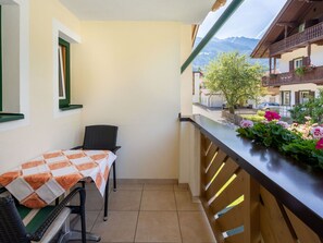 Ein Balkon mit Tisch und Stühlen, Blick auf einen Berg und ein Blumenbeet.