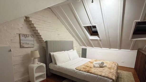 Una camera da letto con un letto, un comodino, una lampada, un quadro e una scala.