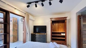Une chambre à coucher comprenant un lit, un téléviseur, une armoire et une porte-fenêtre coulissante donnant sur un balcon.
