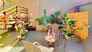 Un espace patio aménagé avec des meubles en osier, une table avec une bouteille et un verre, et diverses plantes en pot.
