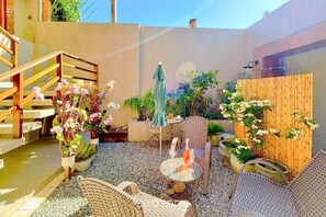 Eine Terrassenanlage mit Korbmöbeln, einem Tisch mit Flasche und Glas sowie verschiedenen Kübelpflanzen.