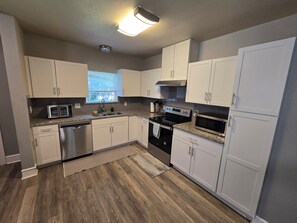A kitchen with white cabinets, stainless steel appliances, and a window with blinds. - The 11th Street Retreat (Temple)