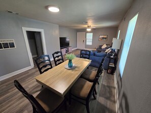 A dining area with a wooden table and chairs, a vase with flowers, and a television in the background. - The 11th Street Retreat (Temple)